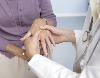 Médico revisando la mano del paciente para determinar el tipo de dolor de la artritis