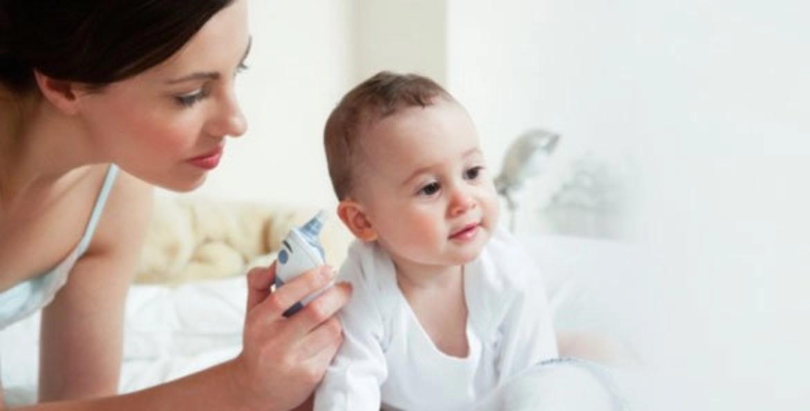 Una madre revisando el oído de un bebé mientras sostiene un termómetro